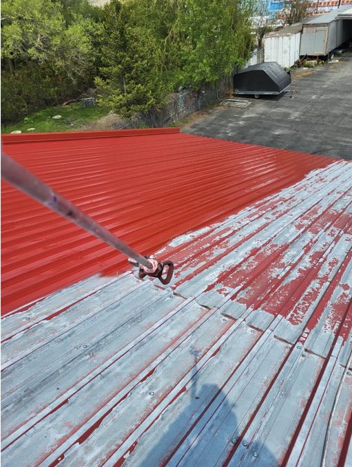 Application de peinture rouge sur une toiture métallique industrielle, à moitié complétée